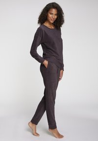 Vijoličen komplet za sprostitev, narejen iz mehke tkanine. Zgornji del ima okroglo izrez, hlače pa imajo elastičen pas in prilegajoče se manšete.