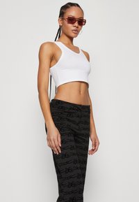 Witte cropped tanktop gecombineerd met zwarte broek met een herhalend patroon. Het model draagt transparante rode zonnebril en heeft gevlochten haar.