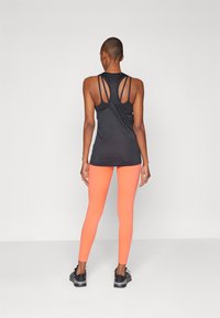 Svart ermeløs treningstop med utskårne ryggstropper, kombinert med tettsittende oransje leggings og svarte treningssko.