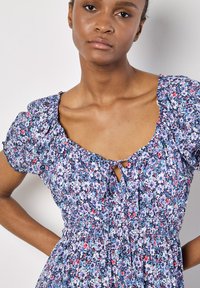 Blumenkleid mit gerafftem Oberteil, Puffärmeln und quadratischem Ausschnitt mit Schlüssellochdetails, hauptsächlich in Blau-, Pink- und Violetttönen.