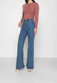 Rosa ribbad långärmad topp i kombination med högmidjade blå utsvängda jeans. Outfiten kompletteras med en vit handväska och öppna vita klackar.