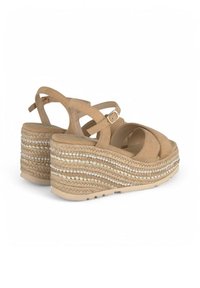 Sandales compensées en suède beige avec des lanières entrecroisées, une plateforme tressée texturée et des accents décoratifs en perles sur les côtés.