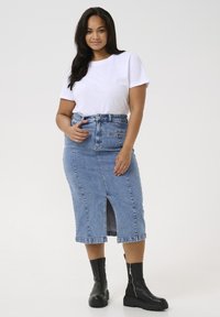 Svetlo modra denim mini krilo s sprednjim razporkom, visokim pasom in zankami za pas, v kombinaciji z belo majico in črnimi gležnjarji.