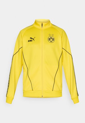 Gul fuld-zip sportsjakke med sort Puma-logo, "KING" tekst og BVB 09 fodboldklub emblem med to stjerner på brystet.