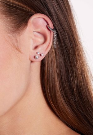 Zilveren oorcuff met een ketting, trio van kleine stud oorbellen: één bolvormig, één met een kristal en één vlak, allemaal met een glanzende afwerking.