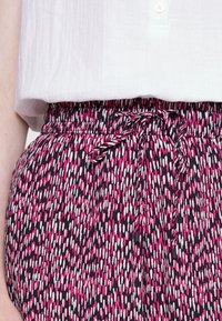 Luźne, wzorzyste spodnie w czarnym kolorze, z różowymi i białymi abstrakcyjnymi wzorami, elastycznym pasem i detalem związanego sznurka.