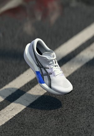 White and black running shoe with blue sole detail floating above an asphalt road marked with white lines.