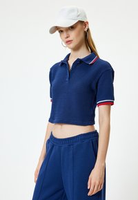 Navy kolorowy polo z krótkim rękawem, wykonany z teksturowanej tkaniny, z zapięciem na guziki przy kołnierzyku oraz akcentami w czerwono-biało-niebieskie paski. Zestawiony z pasującymi niebieskimi dresami.