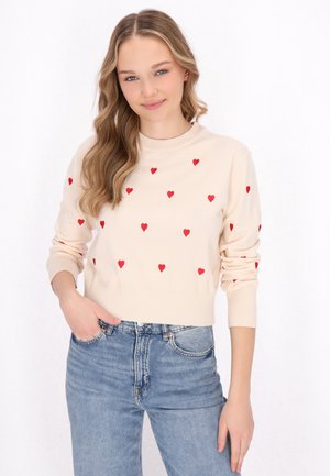 Kermansvärdtröja med röda broderade hjärtan, rund hals, och ribbade ärmslut, parat med högmidjade denimjeans.