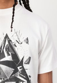 White cotton t-shirt featuring a black geometric graphic design with sharp angles and intricate patterns, emphasizing texture and density.