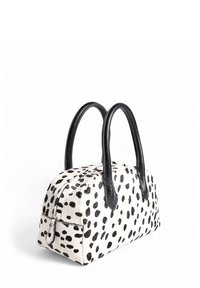 Torebka w cętkowanym wzorze z fakturowanej białej tkaniny w czarne plamy, połączona z eleganckimi czarnymi skórzanymi uchwytami i zamknięciem na zamek.