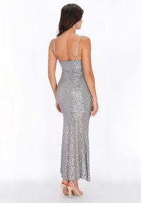 Abendkleid aus silbernen Pailletten mit figurbetonter Form, Spaghettiträgern und ausgestelltem Saum. Glatte Textur mit schimmernden Details durchgehend.