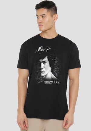 Young man wearing black T-shirt with a grayscale portrait of Bruce Lee and "Bruce Lee" text beneath the image.