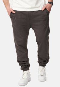 Dunkelgraue Jogginghosen aus weichem Material, mit elastischen Bündchen und Seitentaschen, kombiniert mit weißen Turnschuhen und einem leichten Hemd.