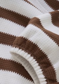 Vaffelstrukturerad tyg med växlande bruna och vita ränder, med en samlad midje detalj och en mjuk, absorberande utseende.