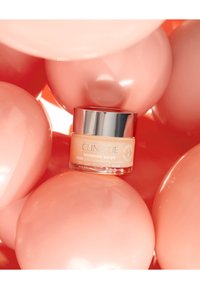 Clinique Moisture Surge krukke, sylinderformet glass, lys ferskenfarget krem, sølvfarget lokk, omringet av glatte, blanke rosa kuler.