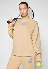 Beige sweatshirt and matching pants, both made of soft fabric. Features a blue and orange Lotto logo on the chest and leg. Tennis racket and ball included.
