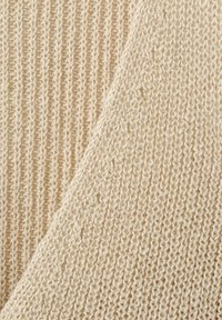 Gros plan d’un tissu tricoté couleur crème montrant deux motifs et textures de tricot différents.