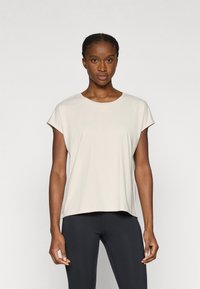 Ανοιχτό μπεζ κοντομάνικο μπλουζάκι με στρογγυλή λαιμόκοψη, λεία υφή και άνετη εφαρμογή, σε συνδυασμό με μαύρο κολάν.