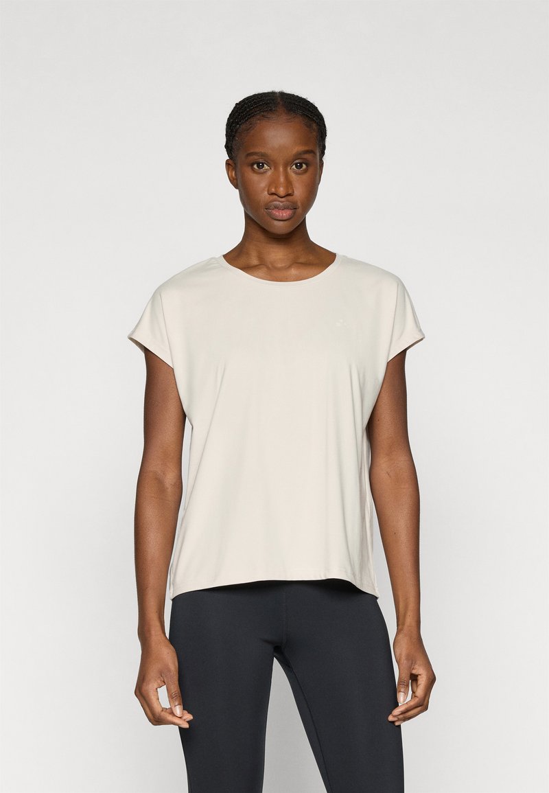 Ανοιχτό μπεζ κοντομάνικο μπλουζάκι με στρογγυλή λαιμόκοψη, λεία υφή και άνετη εφαρμογή, σε συνδυασμό με μαύρο κολάν.