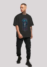 Svart kortermet t-skjorte med en fargerik slange og hodeskalle grafikk. Stoffet virker mykt; løs passform med et minimalistisk design.