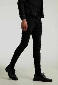 Jeans de mezclilla negros de corte ajustado, con sutiles detalles desgastados, combinados con zapatos de vestir negros brillantes.