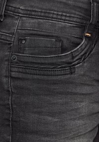Pantalones vaqueros de mezclilla negra con un diseño clásico, que presentan un bolsillo frontal, detalles de costura y una textura suave. Accesorios de hardware mínimos.