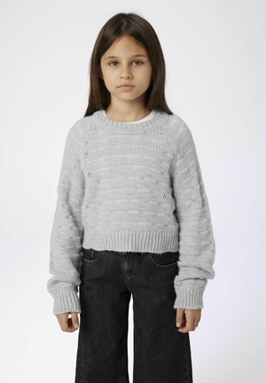 Pull en maille gris clair avec un motif texturé et de larges poignets côtelés, associé à un jean noir taille haute à jambes larges.