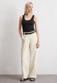 Schwarzes Tanktop, beiger Leinen-Cargo-Hose mit Taschen, schwarzer Gürtel und schwarze Sandalen. Gerades Bein Design, lässige Passform, glatte Textur.