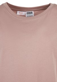 Svetloružové bavlnené tričko s okrúhlym výstrihom, s menovkou značky Urban Classics a štítkom s pokynmi na starostlivosť, na ktorom je napísané "Držte mimo dosahu ohňa."