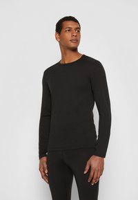 Czarna bluzka z długim rękawem typu crew neck, gładka w dotyku, dopasowany krój, minimalne detale szwowe, w zestawie z czarnymi spodniami.