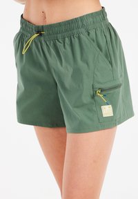 Zelene kratke pantalone izrađene od laganog materijala. Elastična struk sa žutom uže, bočne džepove i mali zip džep sa logom.
