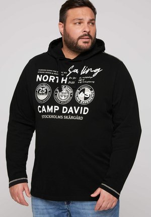 Schwarzer Hoodie mit grafischem Fronttext und Logos. Lange Ärmel haben kontrastierende Bündchen mit silberner Naht. Weicher Stoff. Lässige Passform.