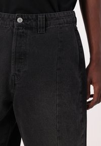 Black denim jeans featuring a fitted design, a standard button closure, and side pockets. The fabric has a smooth, slightly textured finish.