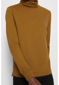 Senfgelber Rollkragenpullover mit langen Ärmeln, aus weichem Stoff gefertigt. Verfügt über ein kleines Leoparden-Print-Logo auf der linken Brust.