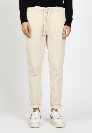 Person wearing beige corduroy pants with drawstring waist, black long-sleeve top, and white Nike sneakers with red swoosh, standing straight.