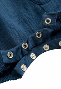 Marineblauwe stof met een gestructureerde oppervlakte, voorzien van zilveren drukknoopsluitingen langs de rand en elastische rimpeling voor flexibiliteit.