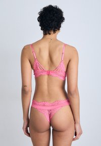 Rosa blonde lingerie-set som inneholder en bralette med justerbare stropper og en matchende tanga. Strukturert blonde med intrikate mønstre og utskjæringer.