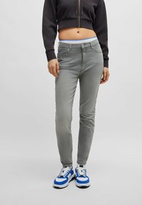 Harmaat slim-fit farkut, joissa on sininen vyötärö, etutaskut ja sileä pinta, yhdistettynä sinisiin ja valkoisiin lenkkarit.