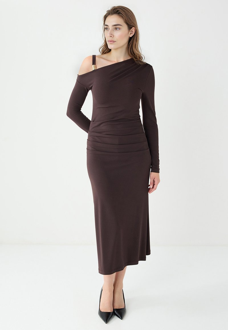 Braunes, schulterfreies Langarmkleid mit körperbetonter Silhouette, Raffung in der Taille und glatter, eleganter Textur. Schwarze High Heels.