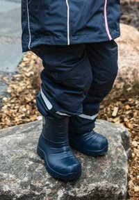 Blå vattentäta stövlar gjorda av gummi, med en strukturerad yta, formade konturer och reflekterande detaljer, placerade på en sten.