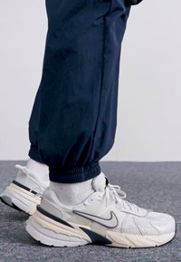 White and grey athletic sneakers with mesh and rubber components. Dark blue cuffed pants, textured fabric, resting on grey carpet.