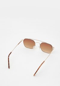 Ochelari de soare cu un cadru din metal auriu, lentile cu gradient maroniu și vârfuri în model țestoasă. Brațe subțiri, unghiulare, design ușor.