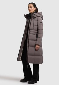 Lang puffer-frakke i lys grå med en afslappet pasform, høj krave, lynlåslommer og kontrasterende inderside med stitch-mønstre.
