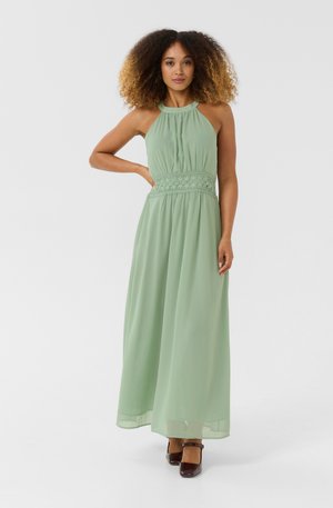 Maxi dress in mint green, sleeveless with a gathered bodice and lace detailing at the waist, flowing skirt, paired with brown block heels.