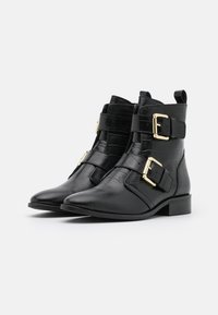 Botines negros hasta el tobillo con textura de cocodrilo, punta afilada, correas con doble hebilla dorada y tacón bajo cuadrado. Acabado liso y construcción robusta.