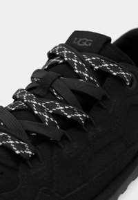 Baskets noires en matériau texturé avec une semelle en caoutchouc. Comprend des lacets à motif noir et blanc, un patch logo et des accents en mesh.