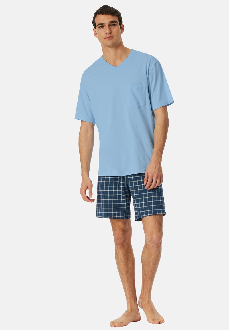 Hellblaues V-Ausschnitt T-Shirt mit Brusttasche, kombiniert mit marineblauen Karoshorts. Das Outfit zeichnet sich durch eine lockere Passform und einen weichen Baumwollstoff aus.