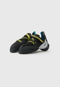 Un paio di scarpe da arrampicata Scarpa Veloce nere e gialle con suole in gomma e cinturini in Velcro su sfondo bianco.