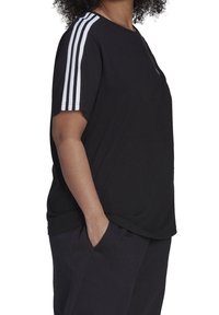 Svart t-shirt med korta ärmar, med tre vita ränder på varje axel. Mjukt tyg med bekväm passform. Fickor syns på byxorna.